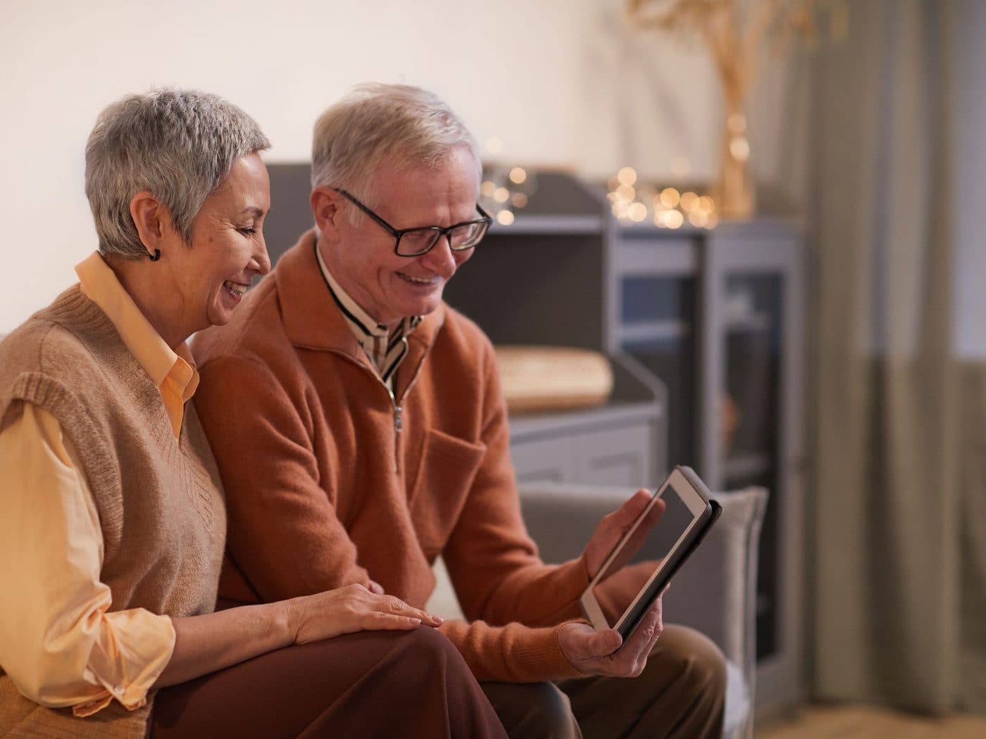 An older couple on their sofa, smiling at a tablet