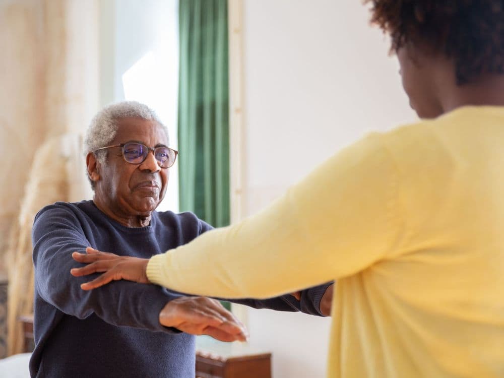 A physiotherapist guiding an older patient through an arm exercise at home